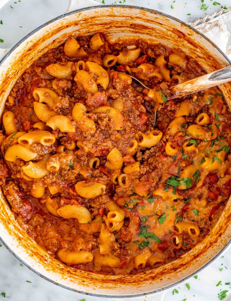 american goulash in a beige dutch oven with a ladle inside.