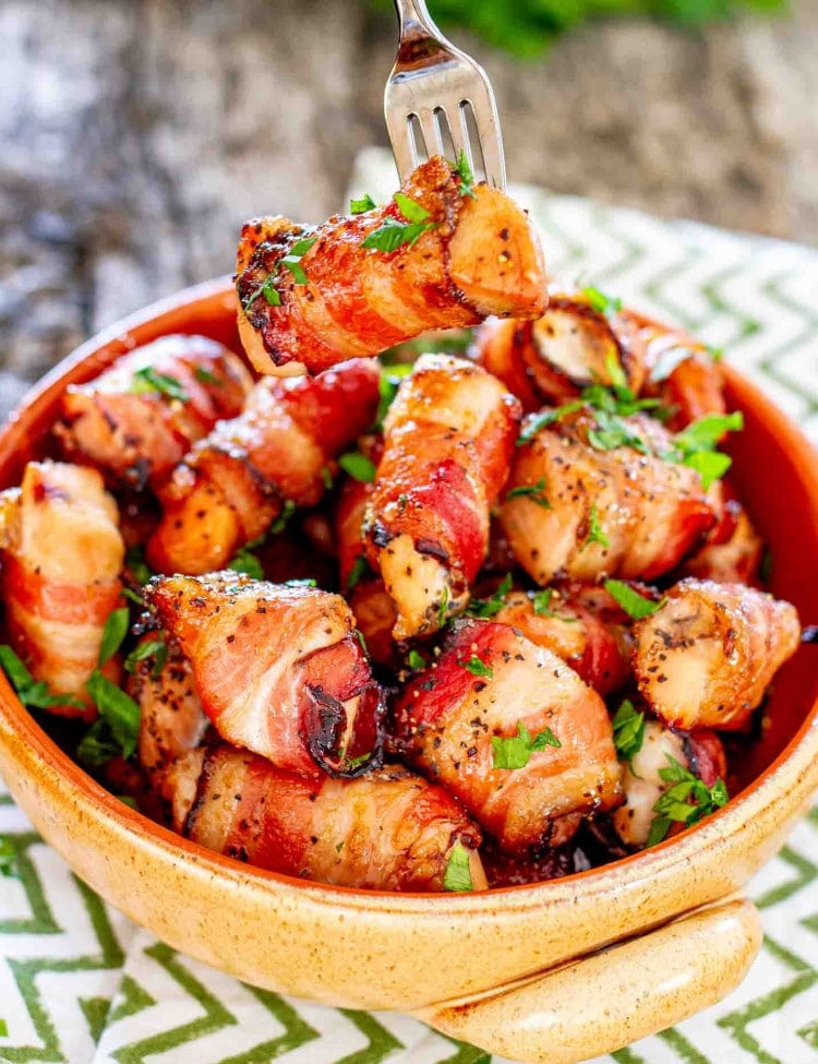 a few bacon wrapped chicken bites in a clay bowl garnished with parsley.