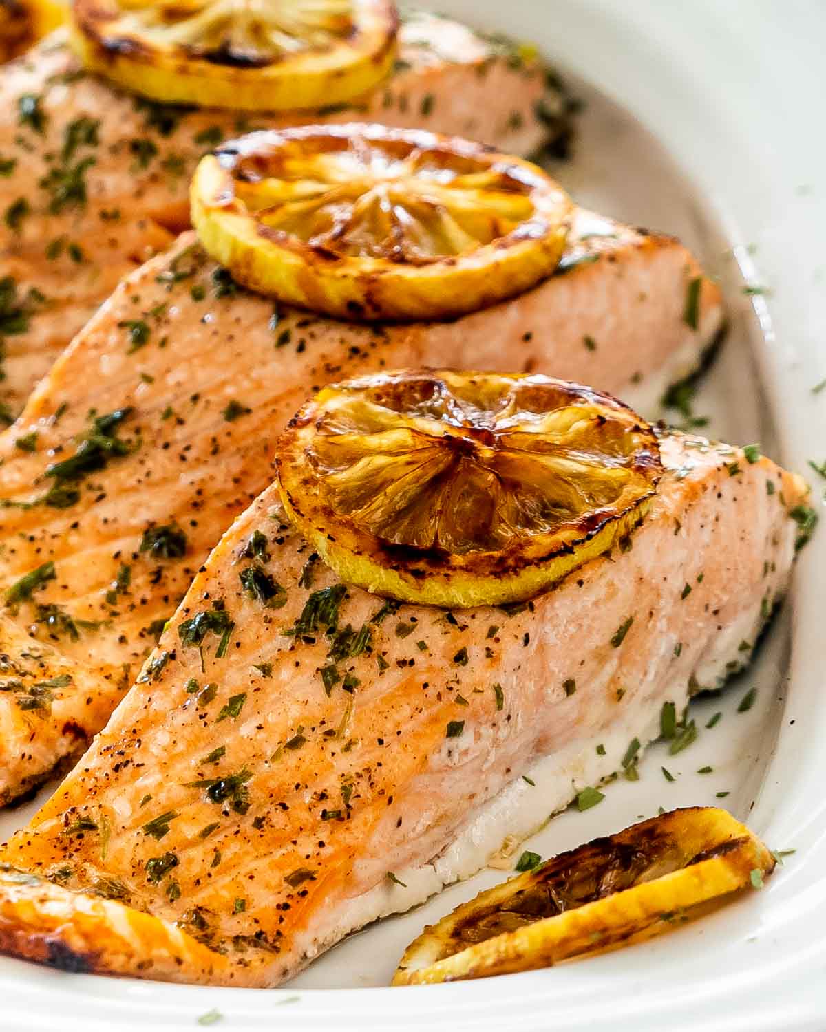 baked salmon with lemon slices on a white platter.