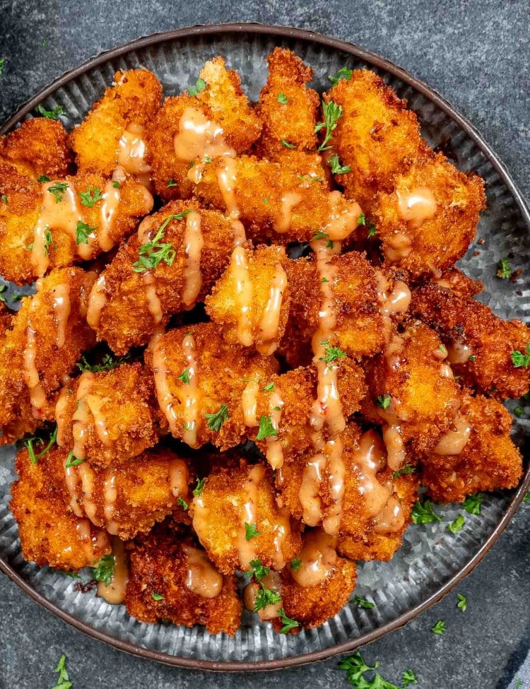a metal plate filled with bang bang chicken, crispy and fried and drizzled with a delicious bang bang sauce.
