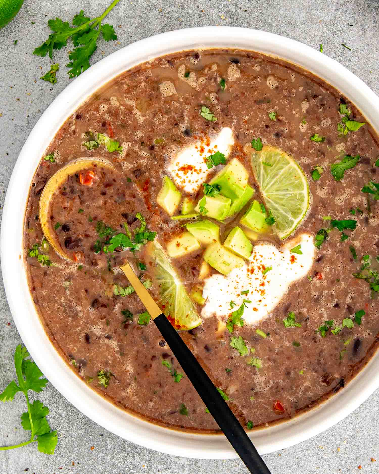 a serving of black bean soup garnished with a dollop of sour cream, cilantro and lime wedges.
