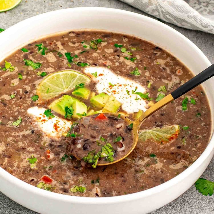 a serving of black bean soup garnished with a dollop of sour cream, cilantro and lime wedges.