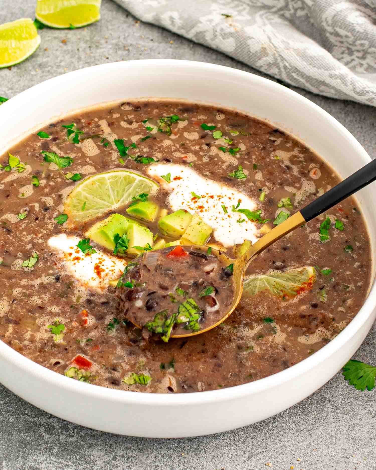 a serving of black bean soup garnished with a dollop of sour cream, cilantro and lime wedges.