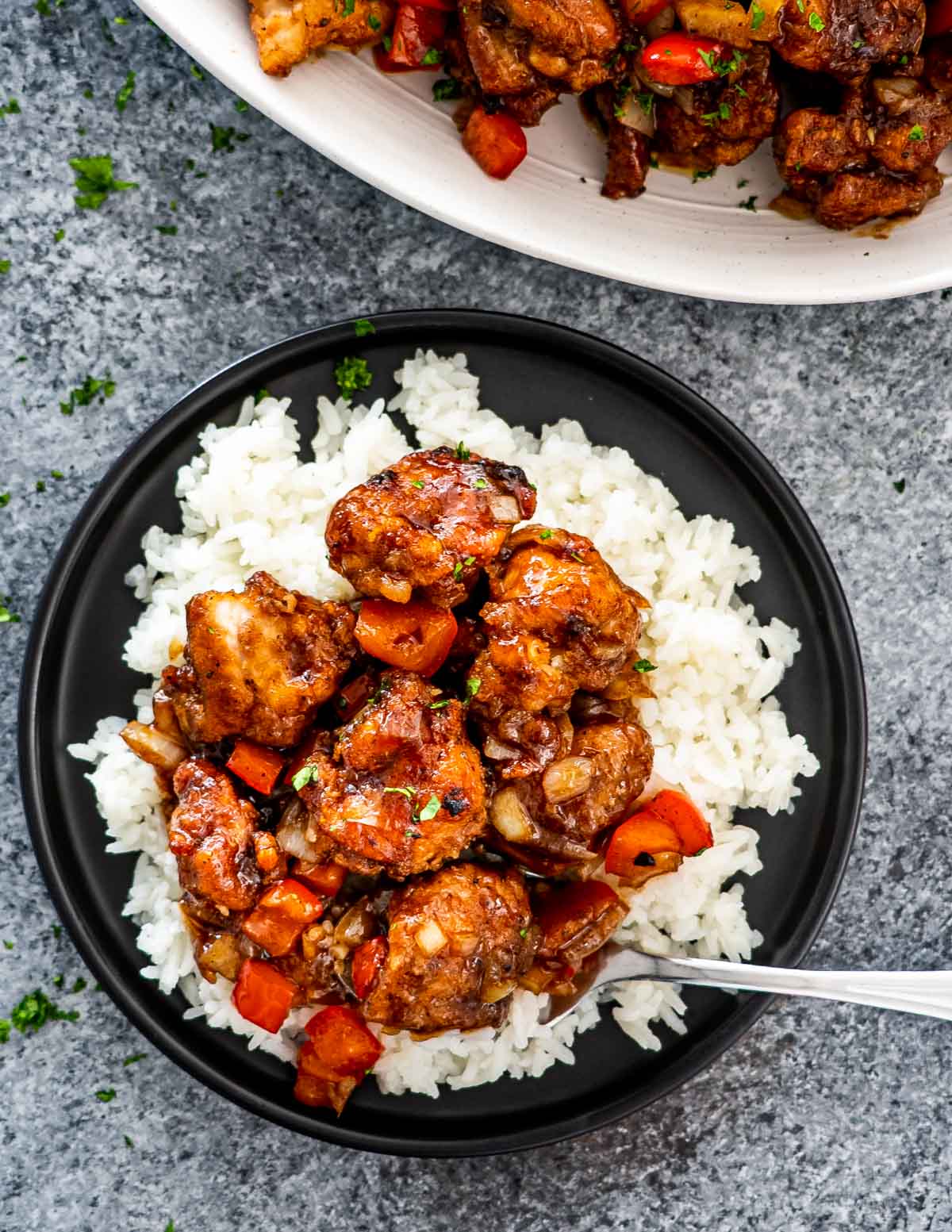 black pepper chicken on a bed of rice on a black plate.