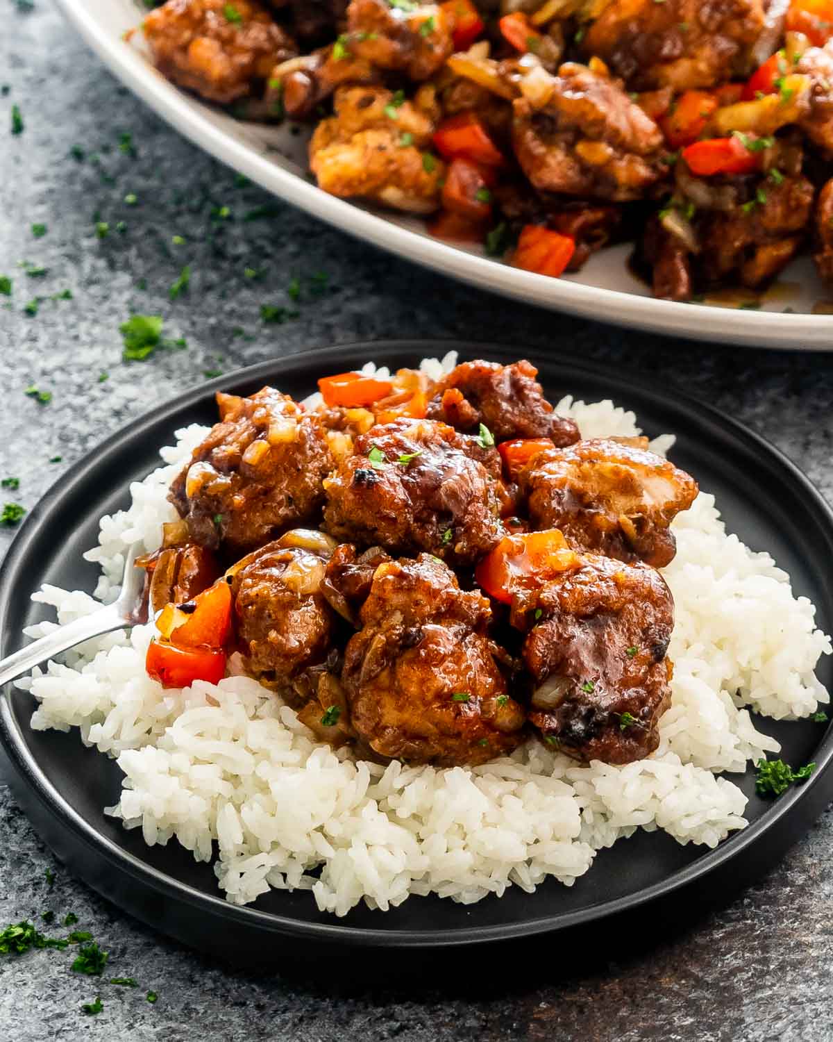 black pepper chicken on a bed of rice on a black plate.