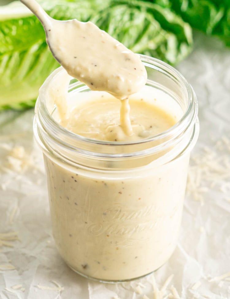 freshly made caesar salad dressing in a jar with a teaspoon inside.