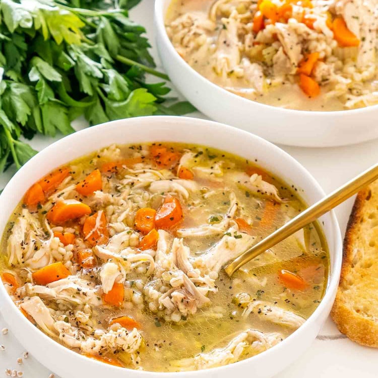freshly made chicken barley soup in a white bowl with a golden spoon in it.