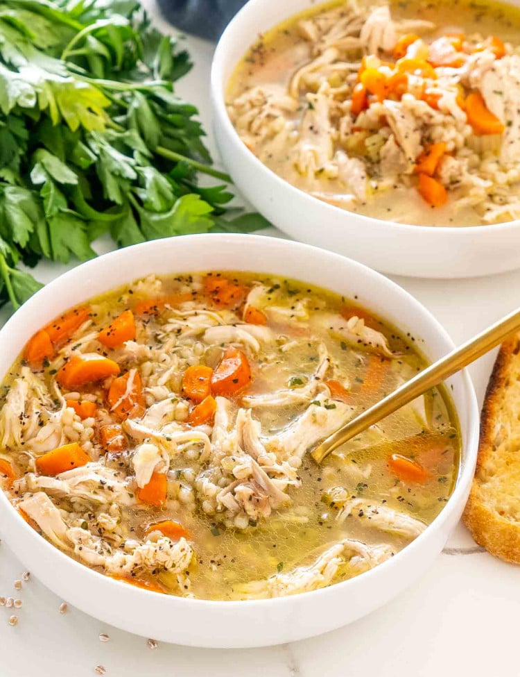 freshly made chicken barley soup in a white bowl with a golden spoon in it.