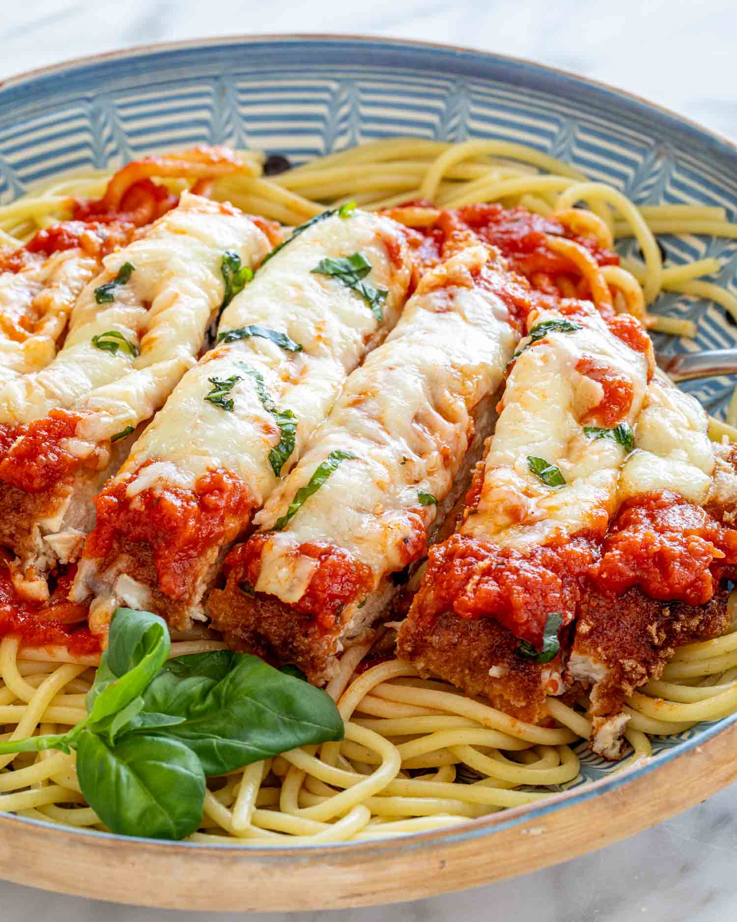 sliced up chicken parmesan on a bed of spaghetti garnished with some fresh basil.