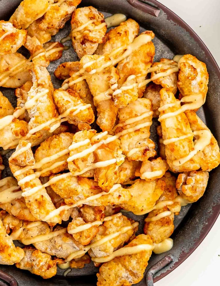 chicken poppers, air fried on a metal plate drizzled with honey mayo sauce.