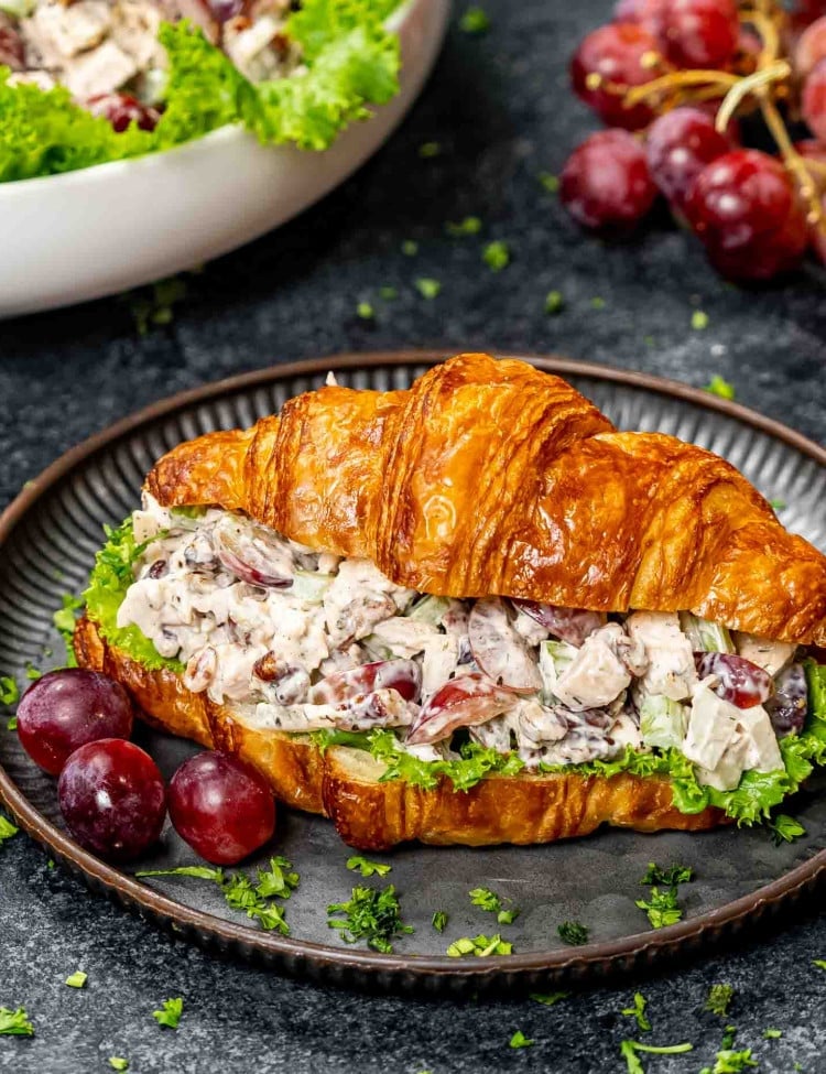 chicken salad on a croissant on a plate with a couple grapes.