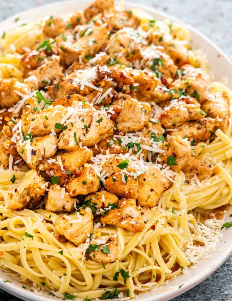 chicken scampi with linguini garnished with parmesan cheese on a white platter.