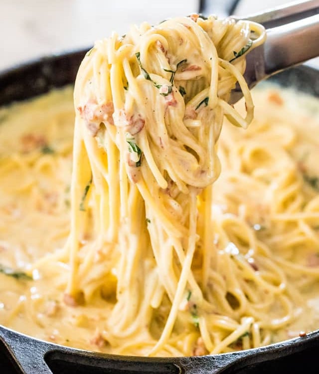 side view shot of tongs holding up some creamy carbonara