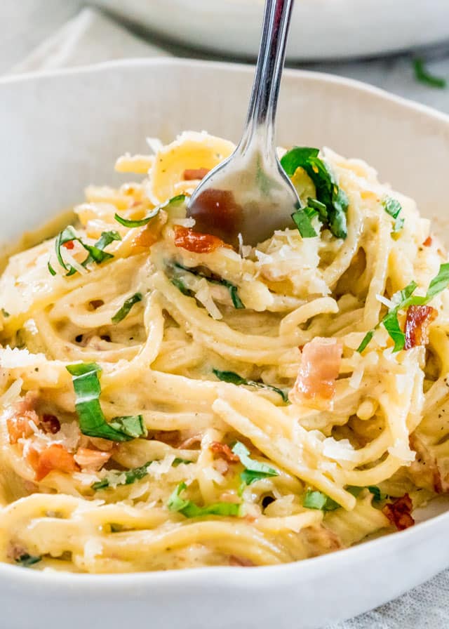 fork twirling creamy carbonara in a white bowl