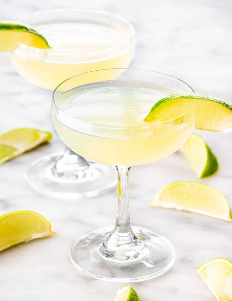 two glasses with daiquiri and garnished with lime wedges.