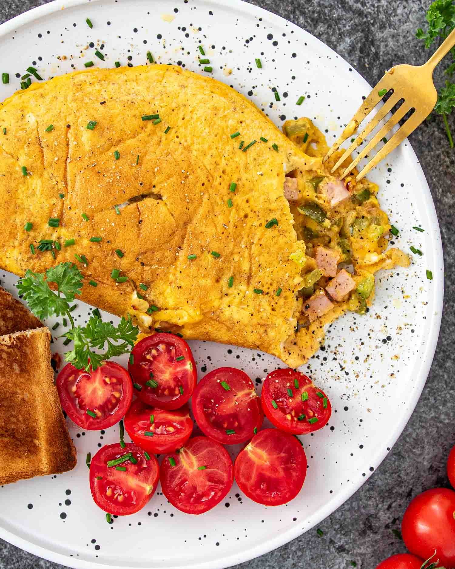 a denver omlette on a plate alongside some cherry tomatoes and toast.