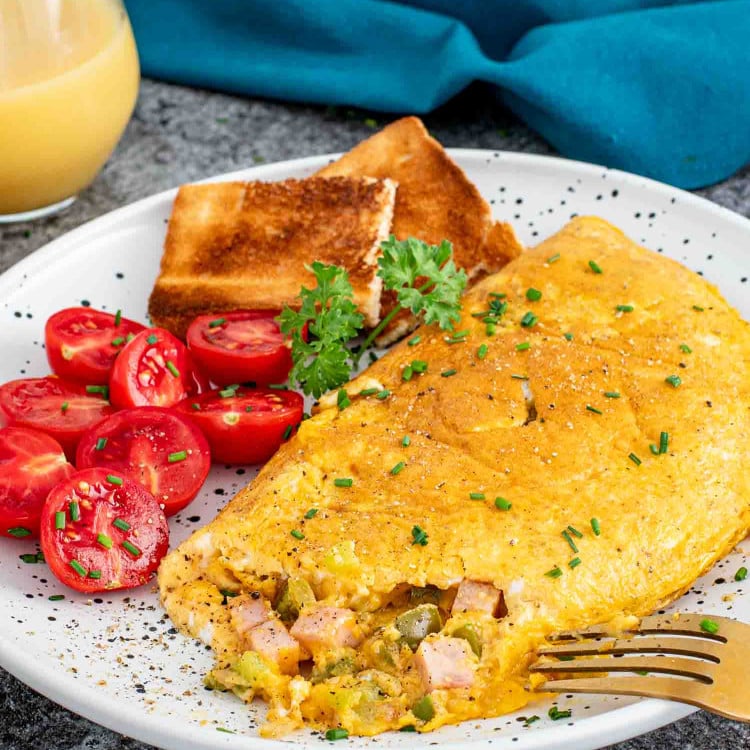 a denver omlette on a plate alongside some cherry tomatoes and toast.