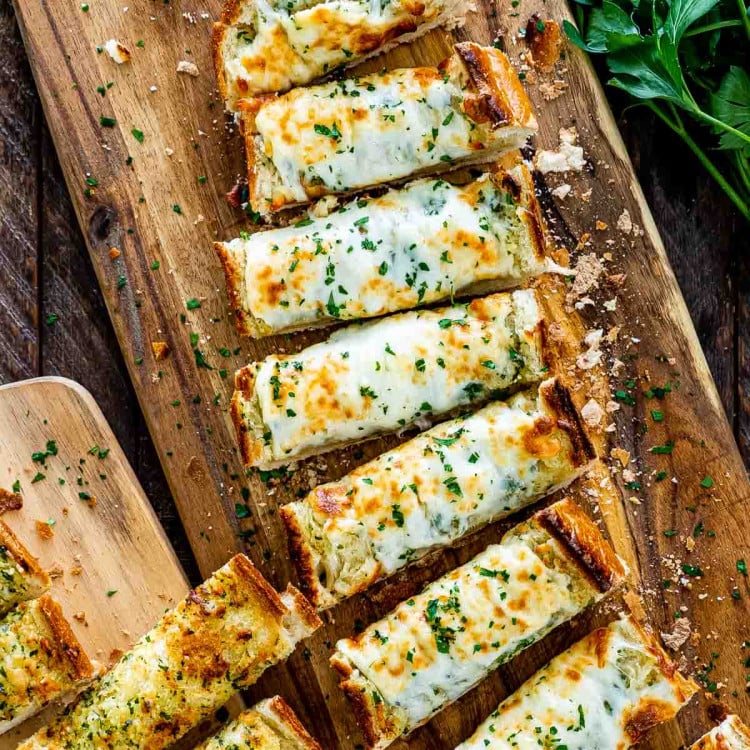 cheesy garlic bread fresh out of the oven sliced on a cutting board.
