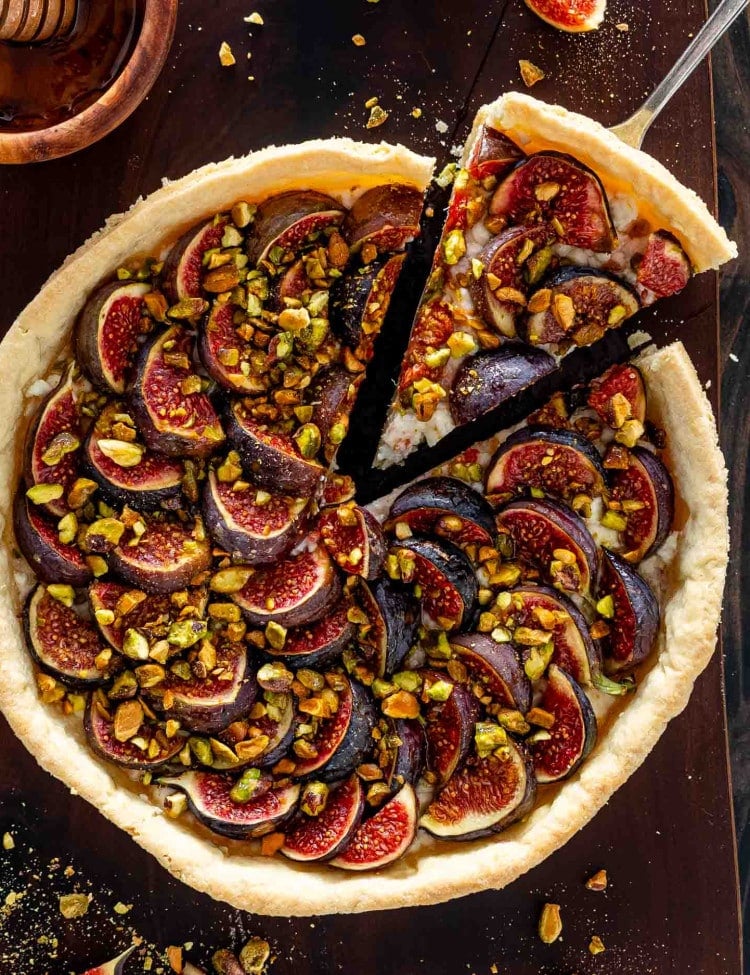a fig tart on a cutting board with goat cheese and pistachios on a cutting board.