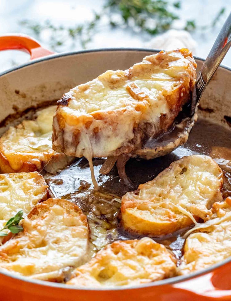 french onion soup in a dutch oven garnished with herbs.