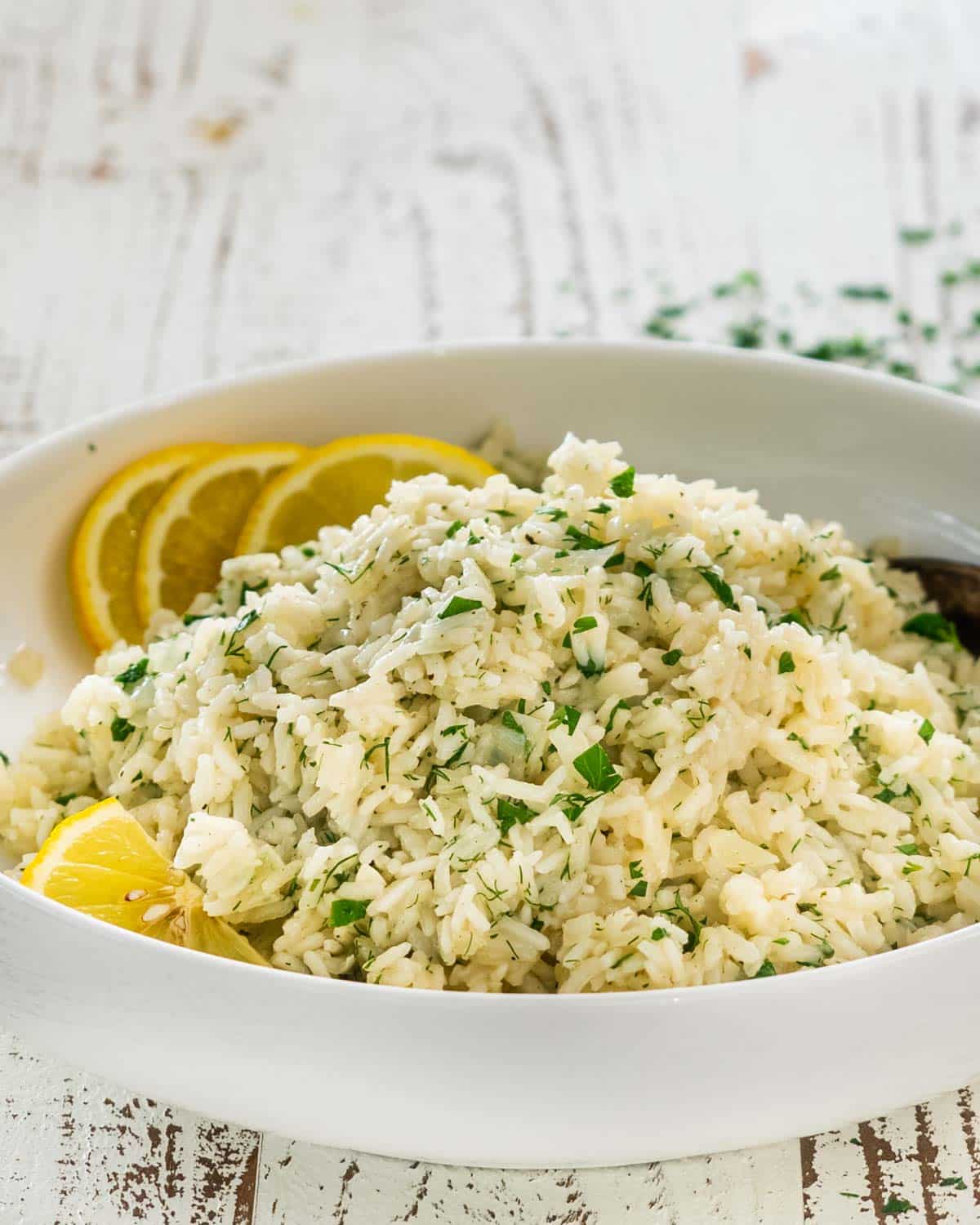 greek rice in a white bowl garnished with lemon slices.