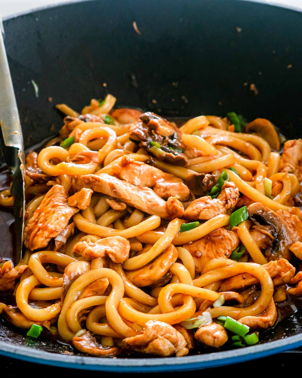sideview shot of hoisin chicken udon noodles in a blue wok