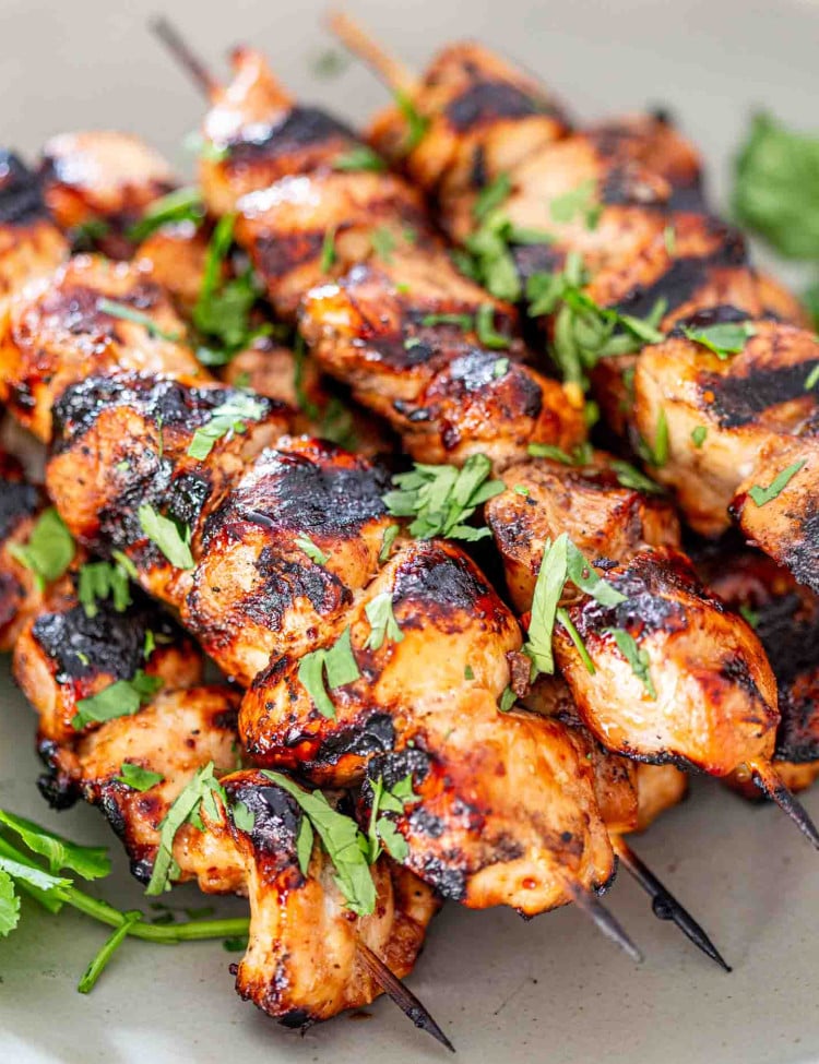 a few honey beer bbq chicken skewers on a white platter garnished with cilantro.