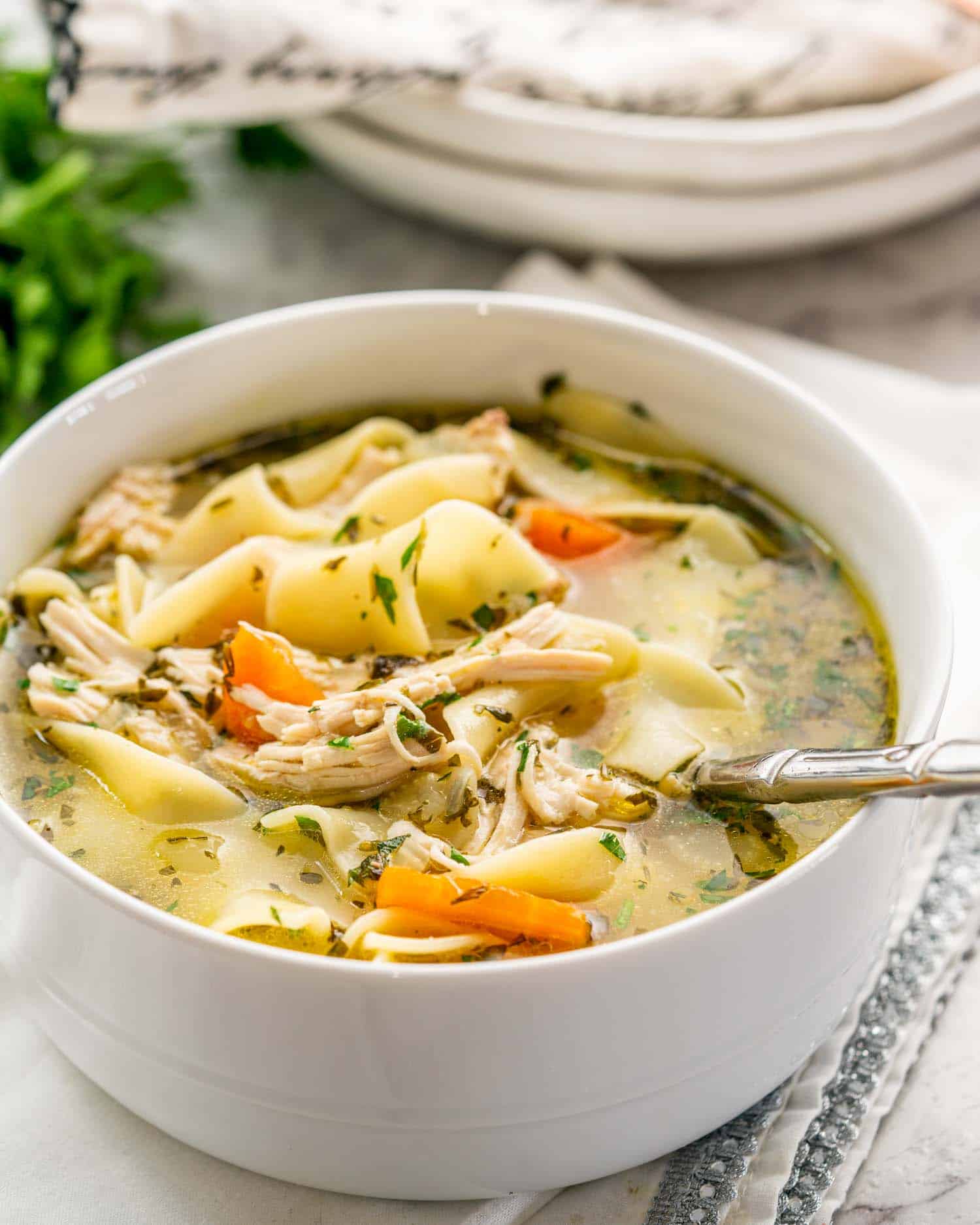 chicken noodle soup in a white bowl with a golden spoon inside.