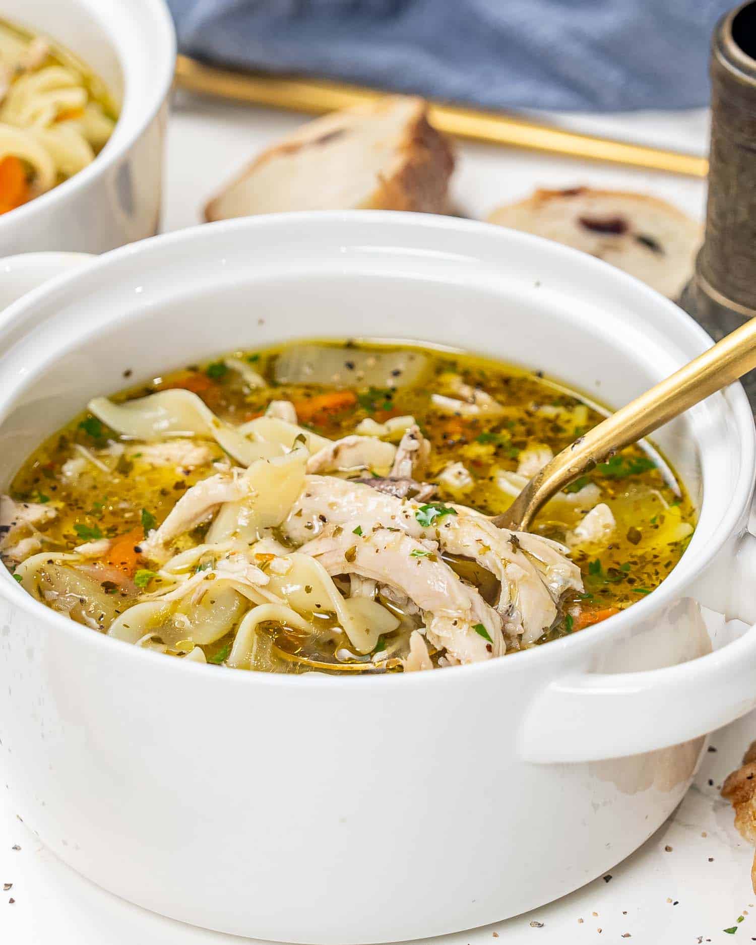 chicken noodle soup in a white bowl with a golden spoon inside.