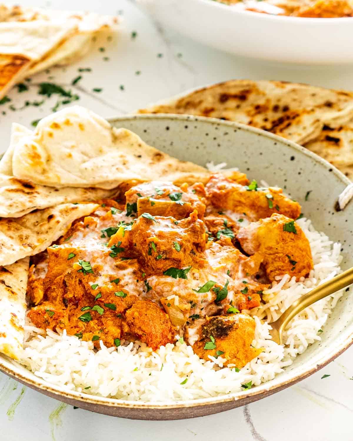 chicken tikka masala in a plate with rice and garnished with cilantro.