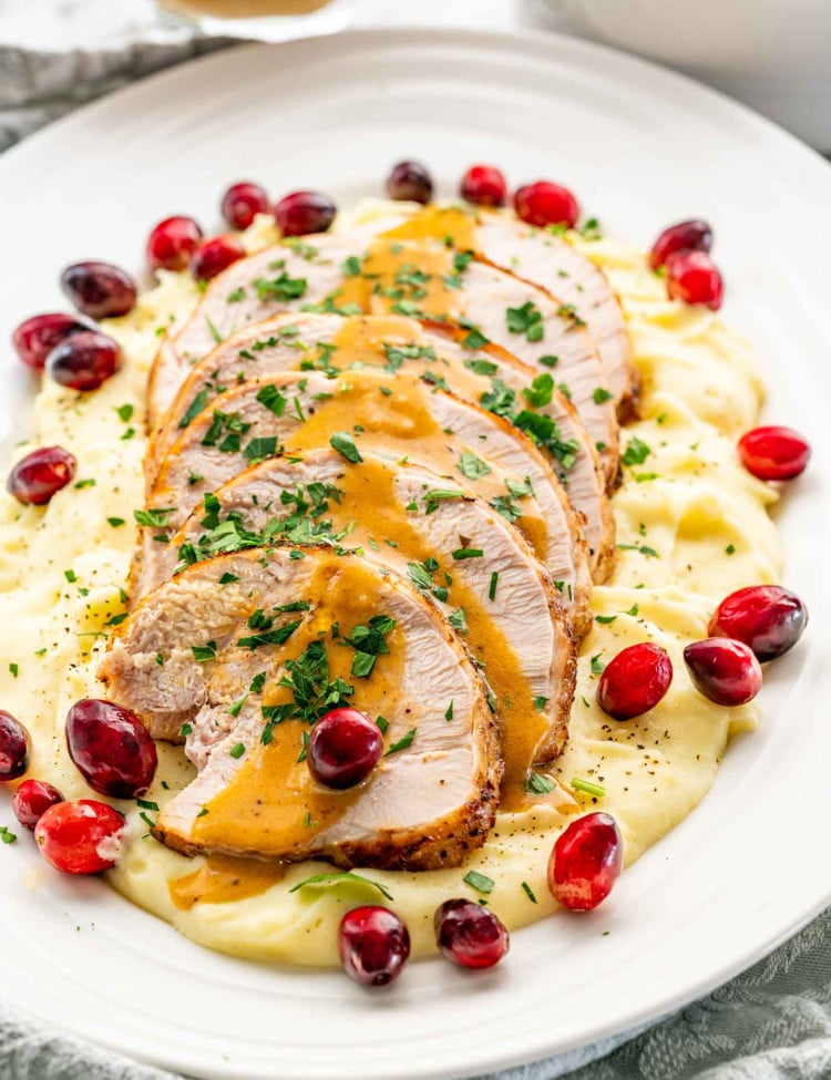 instant pot turkey breast cut in slices over a bed of mashed potatoes garnished with gravy, parsley and cranberries.