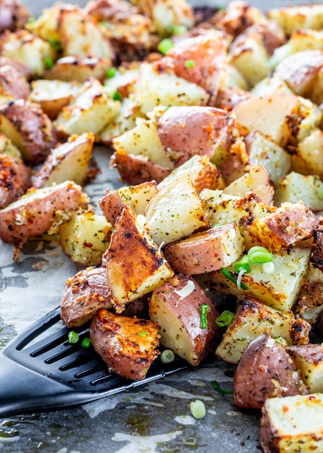 side view close up shot of a spatula grabbing some italian parmesan roasted potatoes from a pan