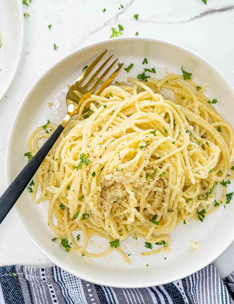 a serving of lemon pasta in a white bowl garnished with parsley and parmesan cheese.