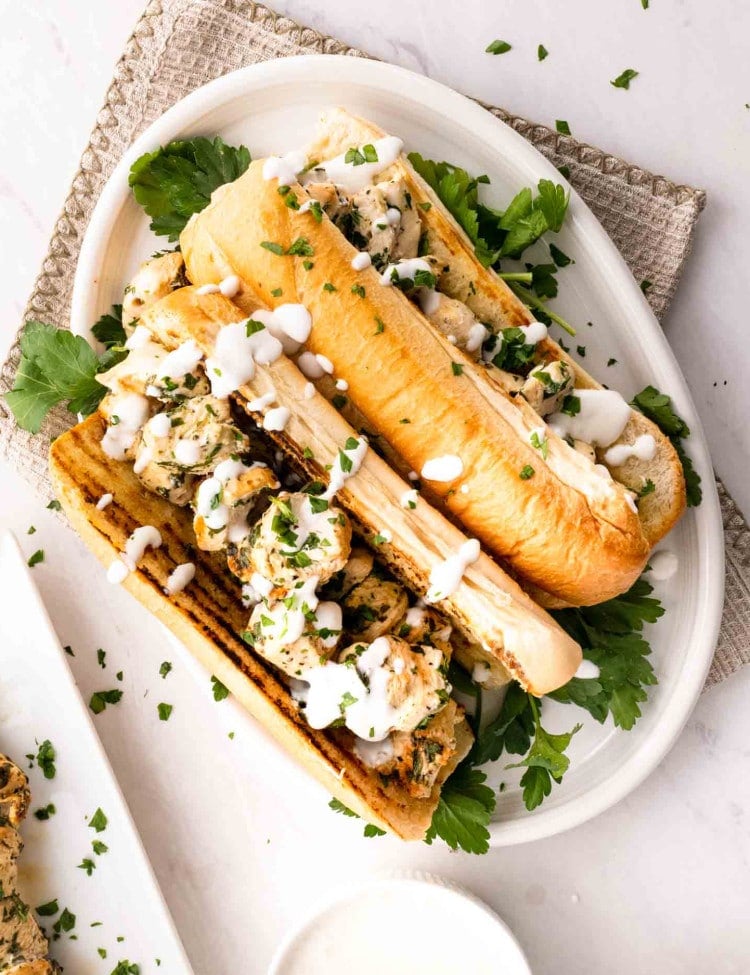 two chicken spiedies on a plate drizzled with garlic sauce.