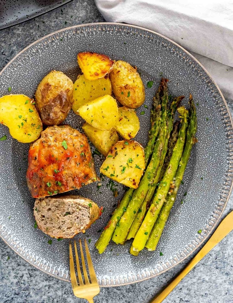 a mini turkey meatloaf on a plate with roasted potatoes and asparagus.