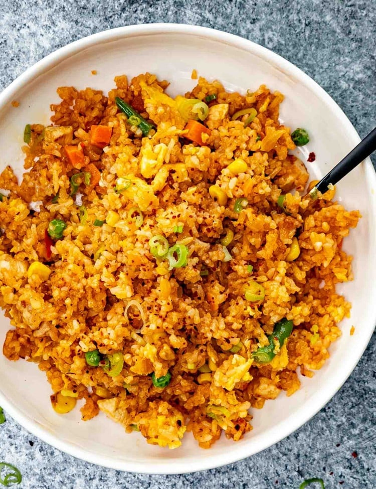 a serving of nasi goreng in a white plate with a spoon inside.