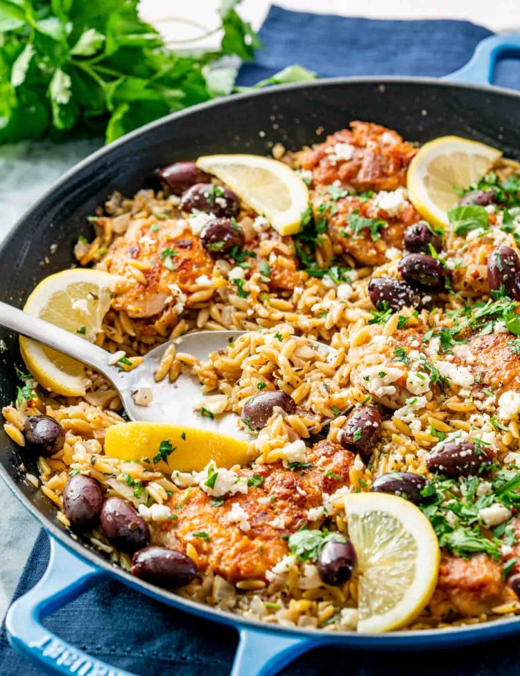 one pot greek chicken orzo in a skillet garnished with lemon wedges and parsley.