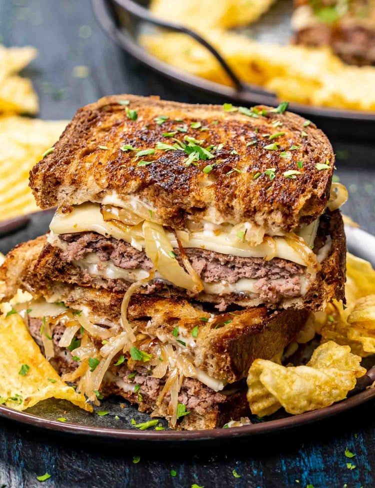 two patty melt sandwiches stacked with potato chips on a plate.