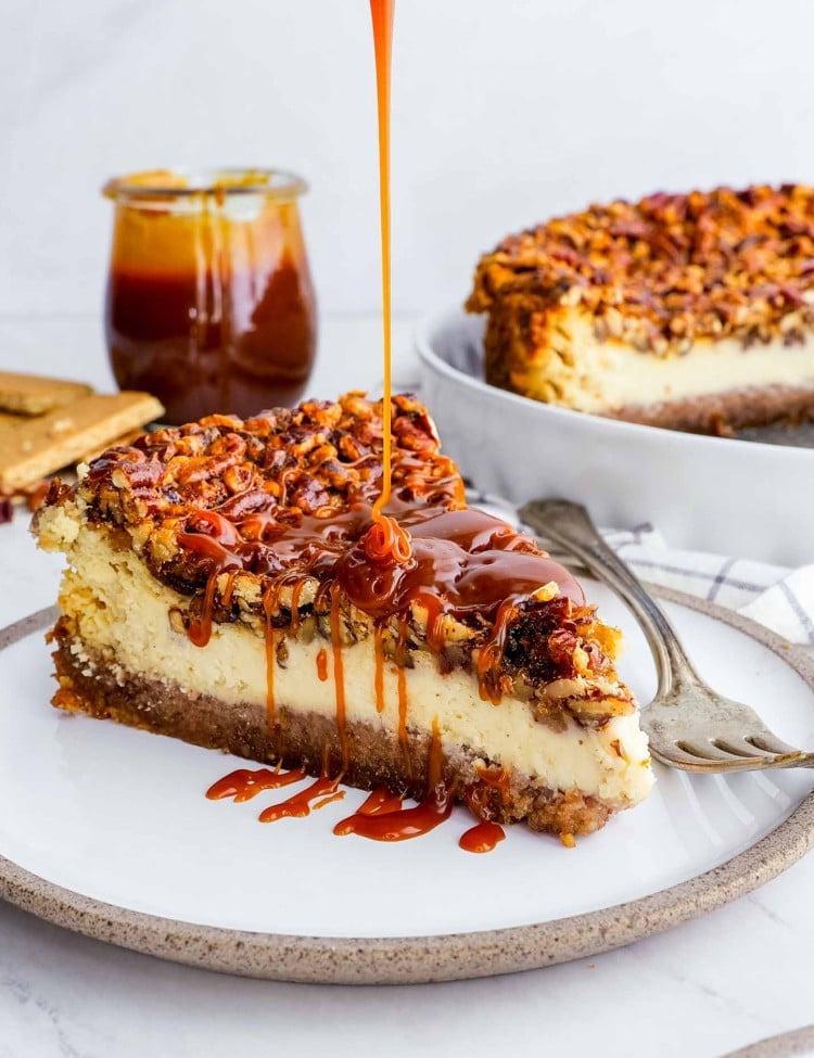 a slice of pecan pie cheesecake drizzled with caramel topping on a white plate.