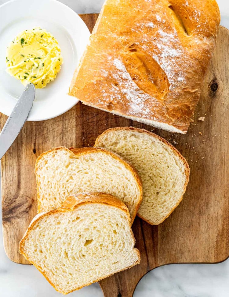 overhead shot of freshly made potato bread on a cutting board with 3 slices a plate with a pat of butter.