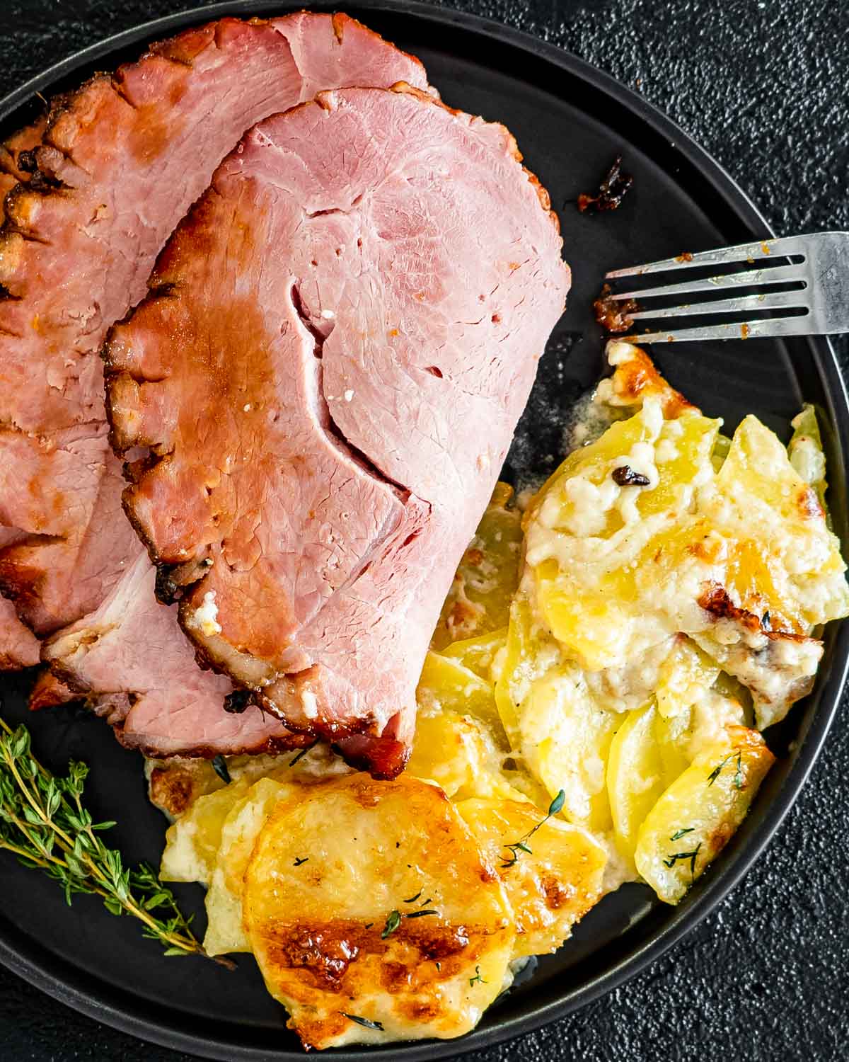 potatoes au gratin with baked ham on a black plate.