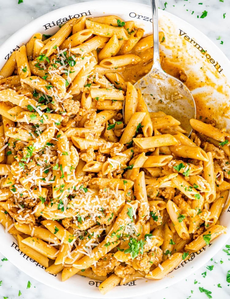 overhead shot of pumpkin sausage pasta in a large serving bowl with a serving spoon taking a scoop