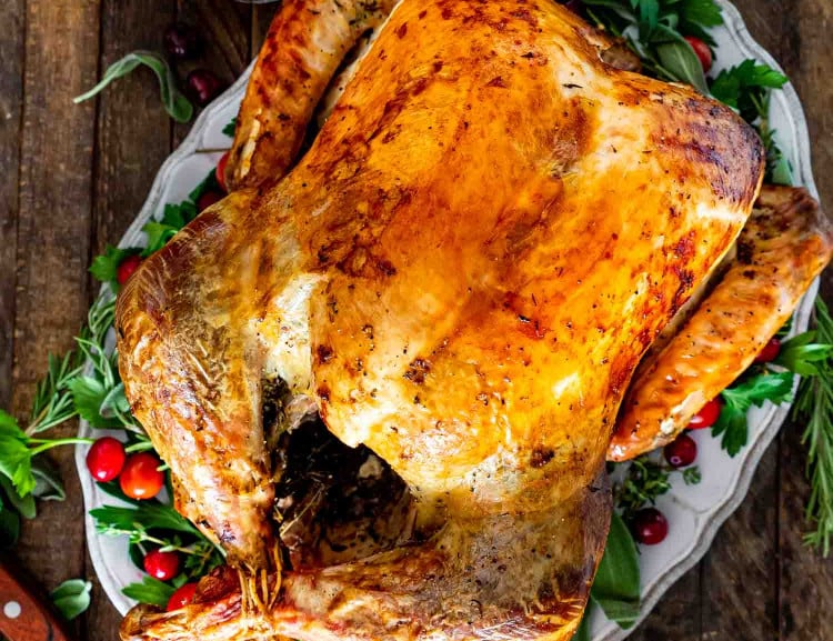a roast turkey on a turkey platter garnished with herbs and cranberries.