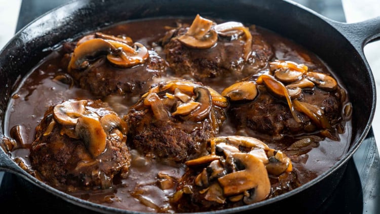 salisbury steak with mushroom gravy in a black cast iron skillet.