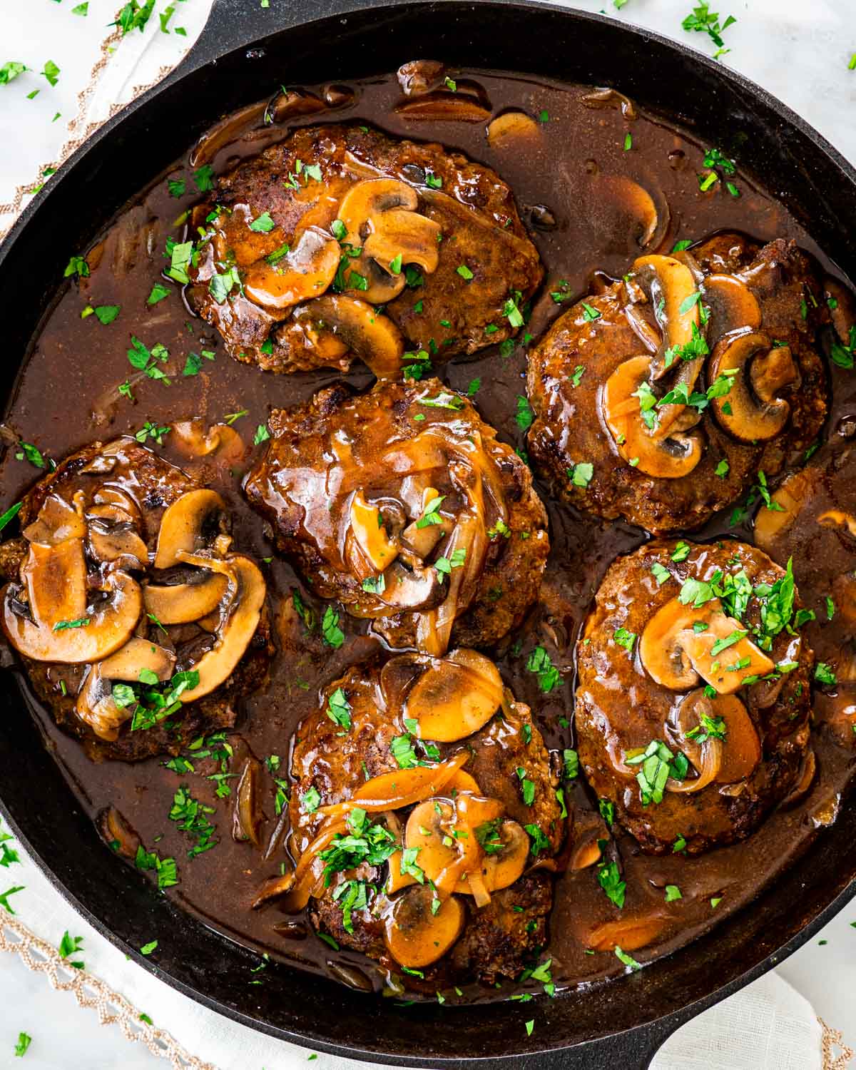 overhead shot of salisbury steak with mushroom gravy in a black skillet garnished with parsley
