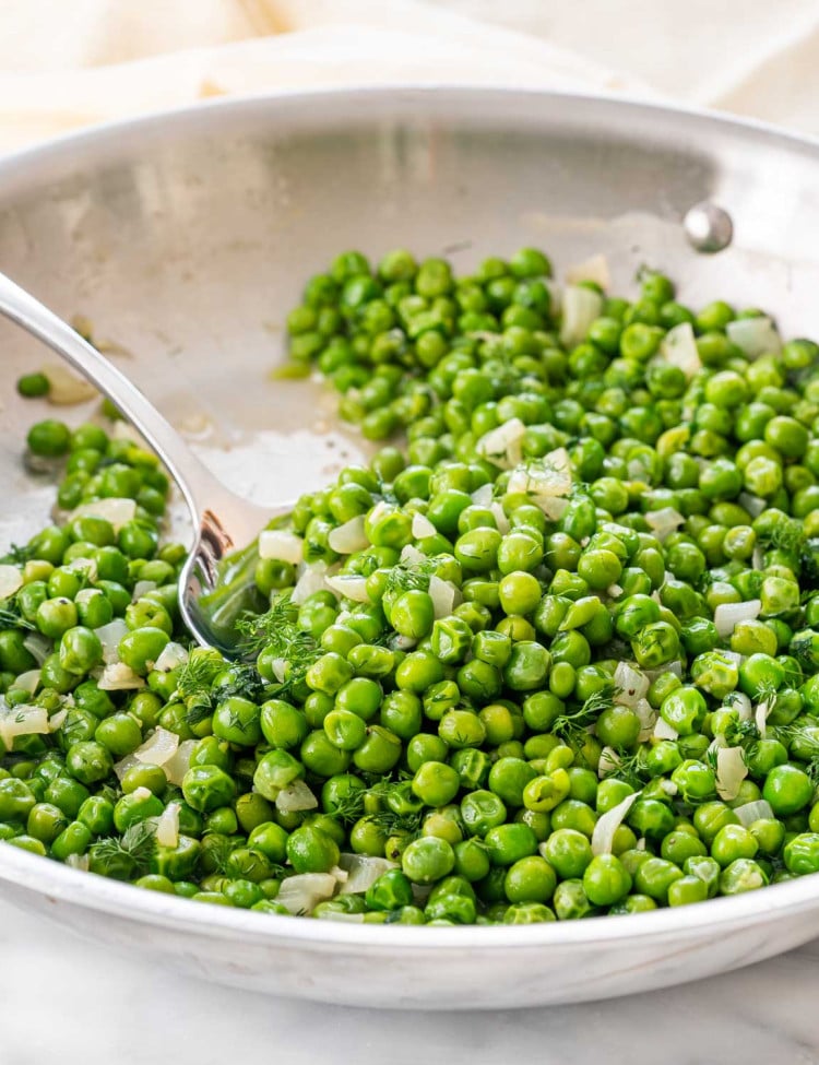 sautéed peas in a skillet with a serving spoon inside.