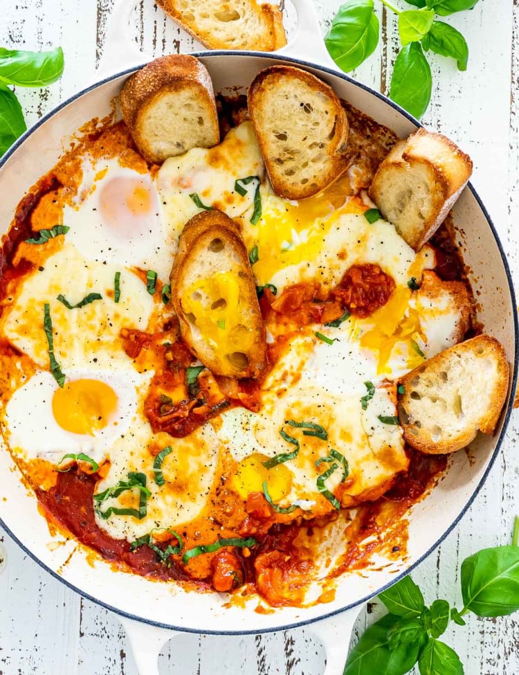 freshly made shakshuka in a beige skillet with some toasted bread.