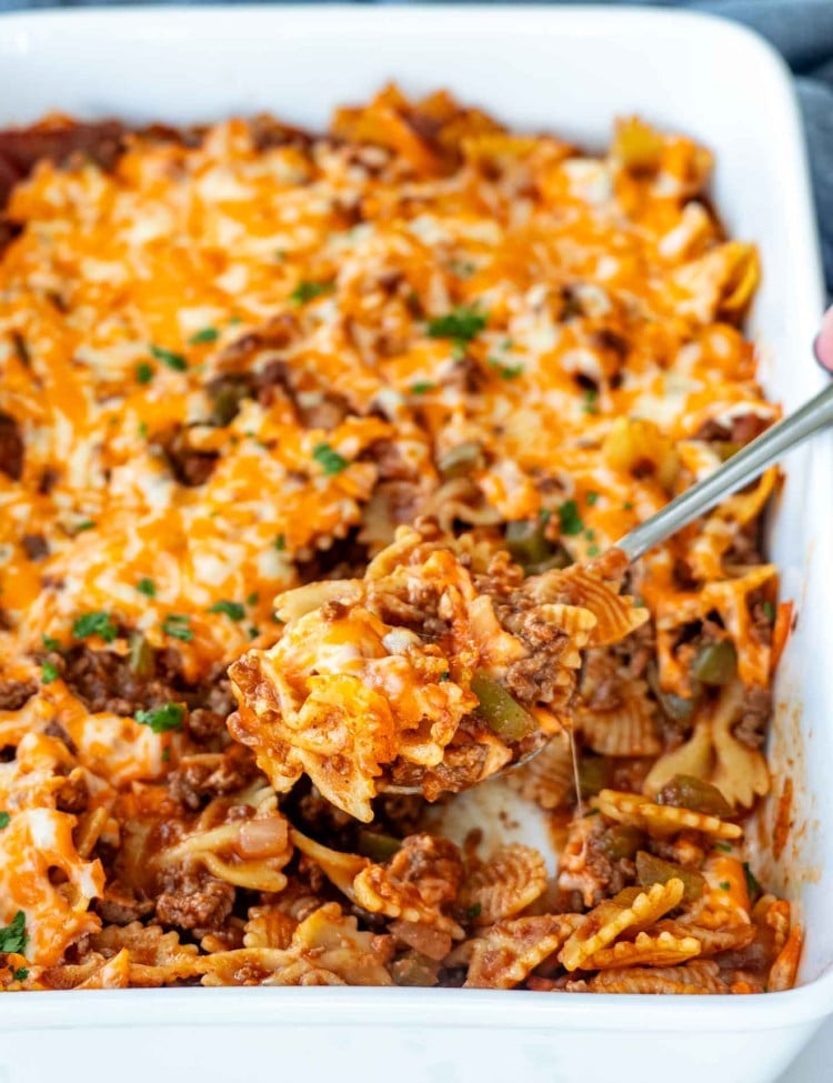 a sloppy joe casserole in a white casserole dish with a serving spoon inside.