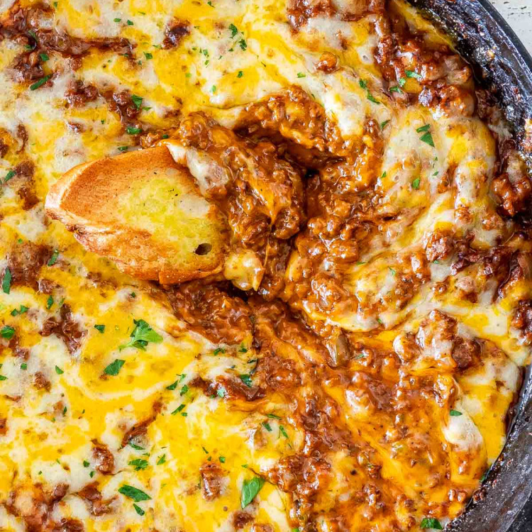 sloppy joe dip in a black skillet with a piece of toasted bread in it.