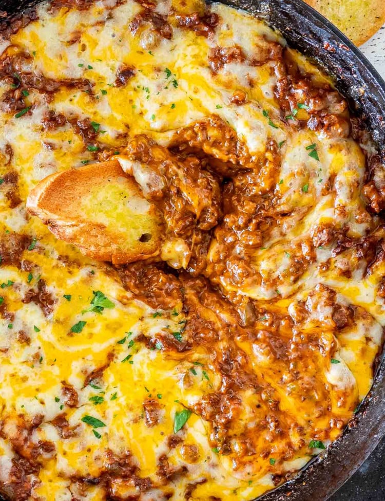 sloppy joe dip in a black skillet with a piece of toasted bread in it.
